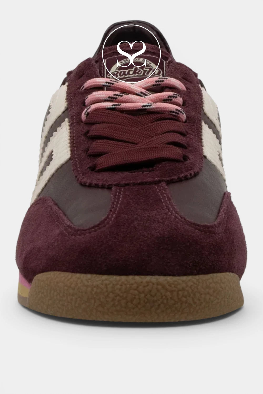 A close-up of a low-top sneaker in burgundy suede and dark brown panels, featuring light pink laces, cream side stripes, and a brown gum sole.